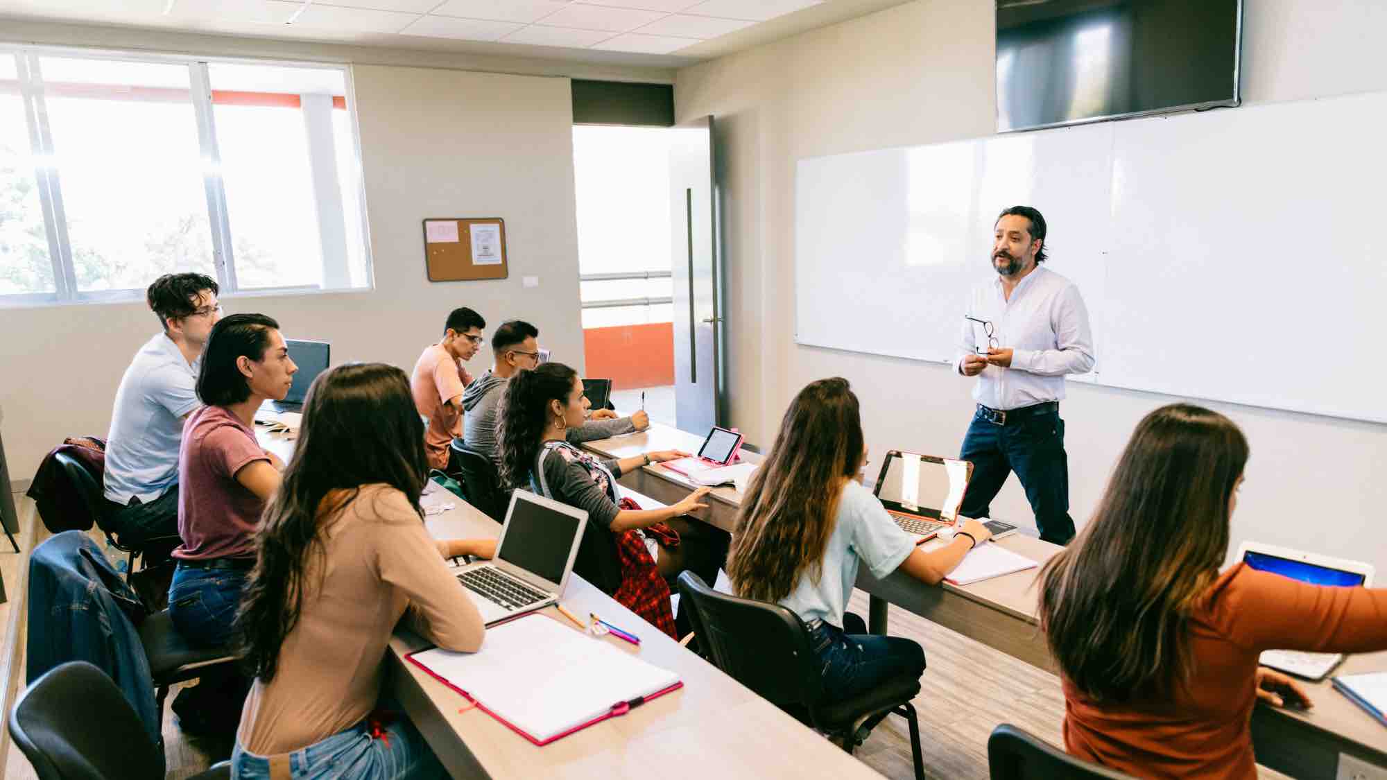 university classroom with instructor standing at the front and students at rows of tables